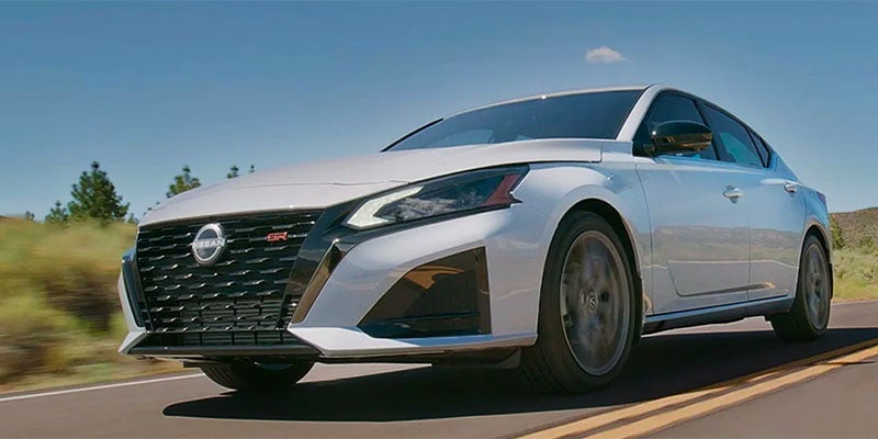 A gray altima driving on a road.