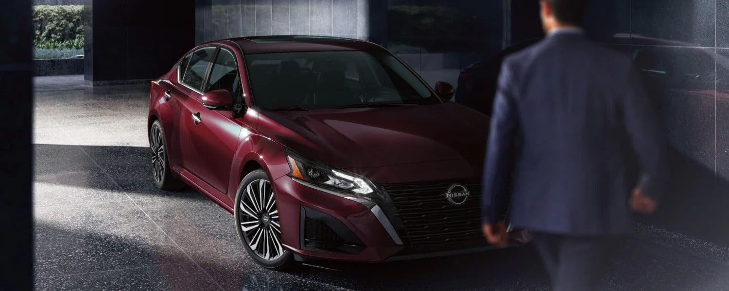 A man walking towards a maroon car.
