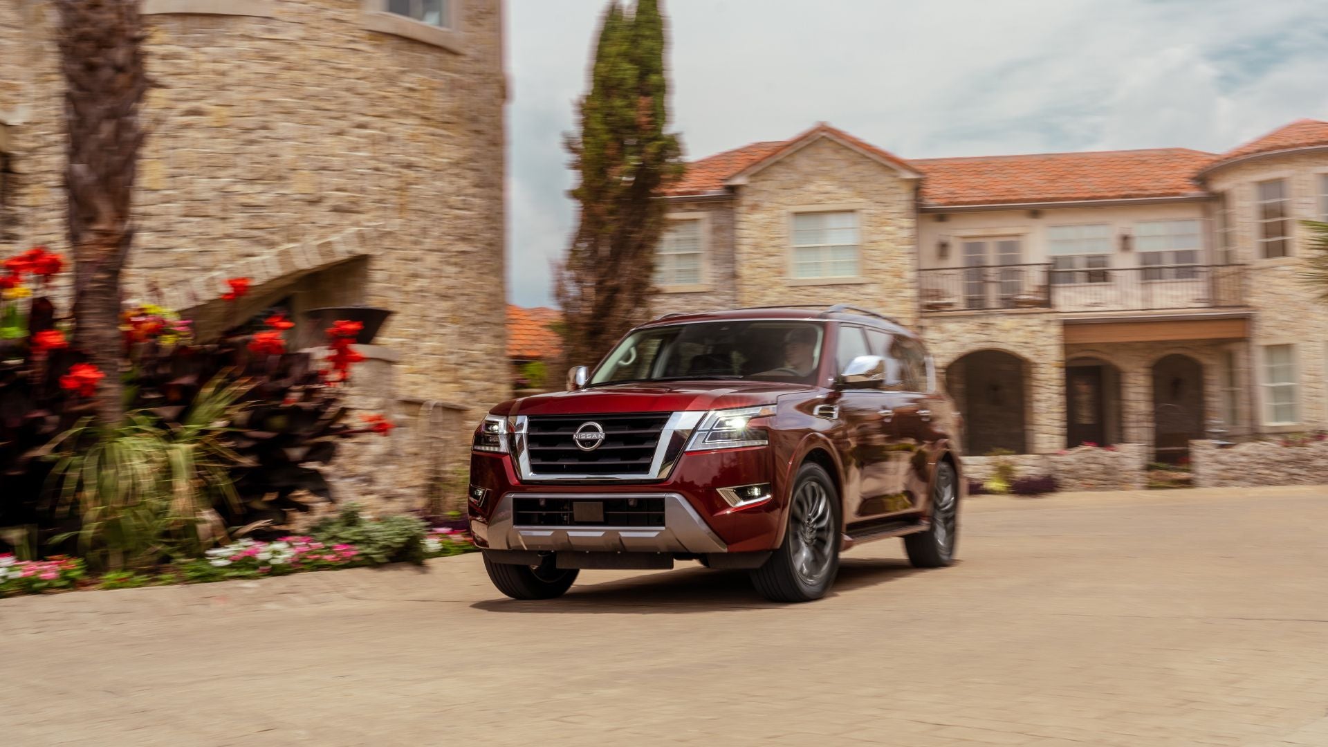 A 2024 burgundy Nissan Armada driving down a Italian villa style street.