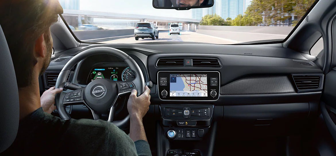 A driver using advanced technology features inside the 2025 Nissan Leaf, showing a touchscreen navigation display and digital dashboard.