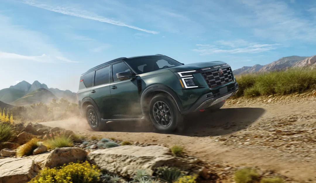 2025 nissan armada 3 row suv driving on a dirt path in the woods