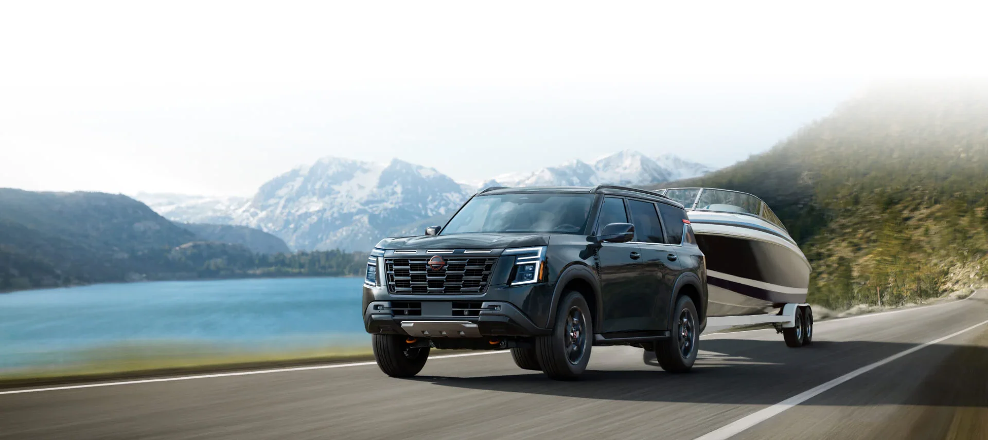 a nissan armada towing a speed boat near the mountains and a lake