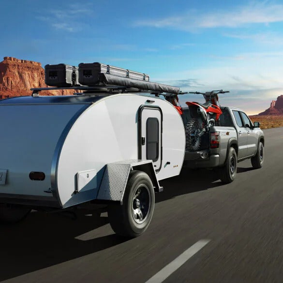 2025 Nissan Frontier towing a teardrop trailer and dirt bike in a scenic desert landscape, highlighting its towing capacity and adventure-ready features.