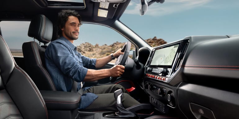 Man driving the 2025 Nissan Frontier, highlighting the modern interior with a touchscreen display and premium seating.