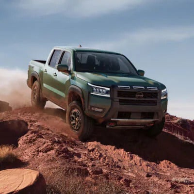 2025 Nissan Frontier climbing a steep, rocky hill, showcasing its off-road technology and rugged performance.