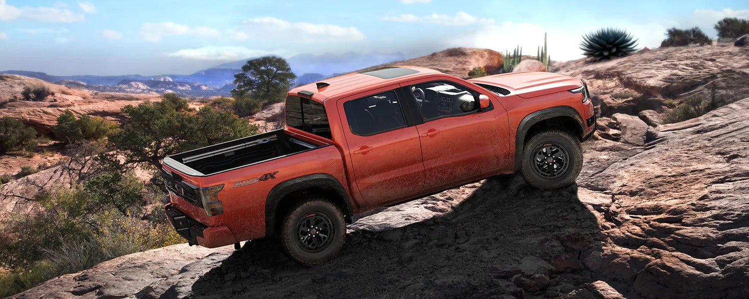a red nissan frontier driving up a rocky terrain